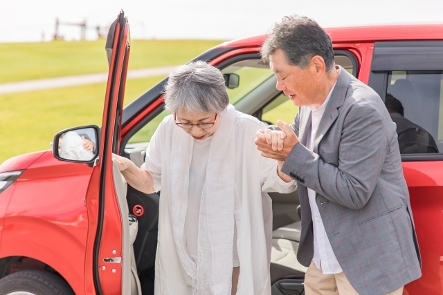 自動車から降りる高齢者女性と介助する男性