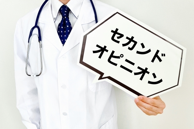 聴診器を首にかけた白衣の男性医師がセカンドピニオンと書いた札を持っているところ、セカンドオピニオンについて説明するイメージ
